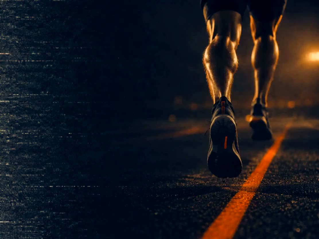 A runner's legs on a dark lane at night, one orange line marking the lane ahead
